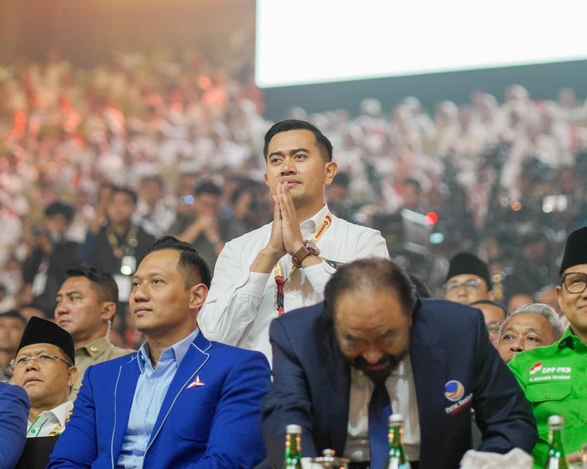 Gugum Ridho Putra berdiri mengatupkan kedua telapak tangan di tengah jajaran ketua umum partai pada sebuah acara kenegaraan.